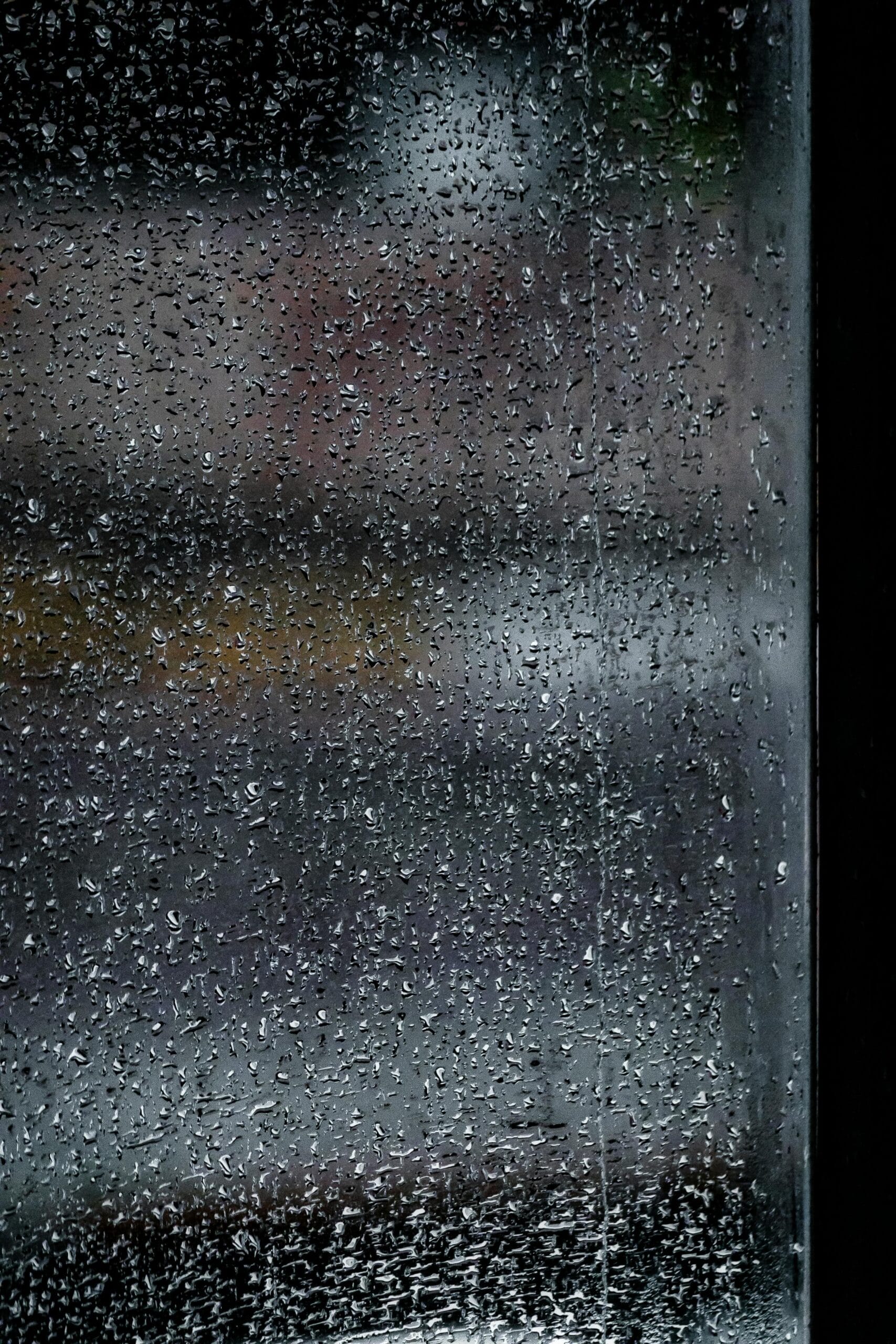 Detailed close-up of rain droplets on a window, creating a moody effect.